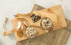 two bowls of oatmeal and an apple on a cutting board