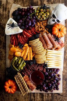 a platter filled with cheese, crackers, grapes and other foods on top of a wooden table