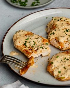 three pieces of chicken covered in gravy on a white plate with a fork