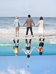 three people holding hands while standing on a beach with their reflection in the water,