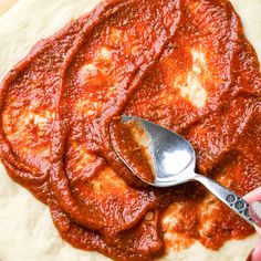 a pizza with sauce on it and a spoon sitting on top of the pizza dough