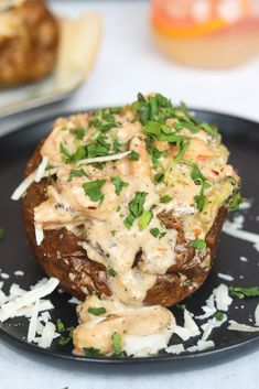 a black plate topped with a baked potato covered in cheese and sauce on top of shredded parmesan