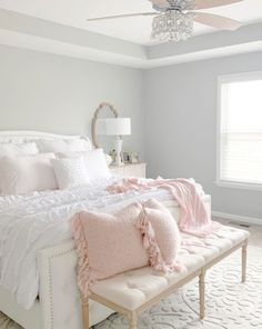 a white bed sitting in a bedroom next to a window with a chandelier