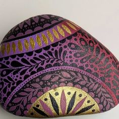 an artistically painted rock with gold and purple designs on the rocks is displayed against a white background