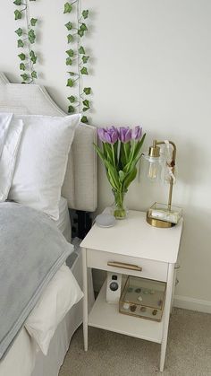 a white nightstand with purple flowers on it next to a night stand and bedding