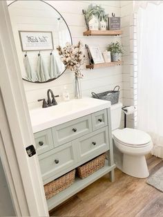 a white toilet sitting next to a bathroom sink under a mirror on top of a wooden floor