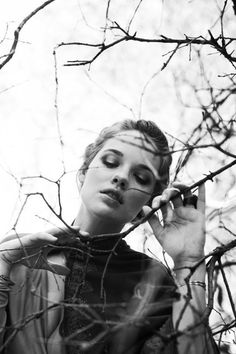 a black and white photo of a woman talking on a cell phone with branches in the background