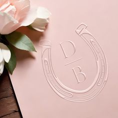 a pink paper with the letter b on it next to some flowers and a pen