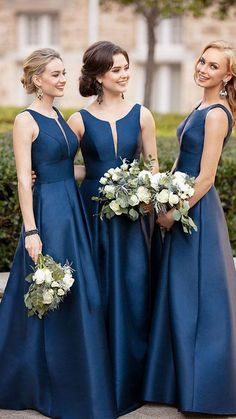 three women in blue dresses standing next to each other with flowers on their bouquets