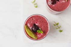 two glasses filled with smoothie and garnished with cherries, lime and mint