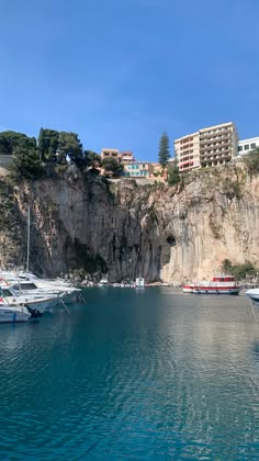 several boats are docked in the water next to a rocky cliff and buildings on top of it