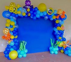 an arch made out of balloons with fish and sea animals on it, sitting in front of a blue wall