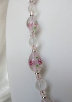 "This lampworked pink jewelry set is made with 14mm round frosted ovals with pink inlaid flowers. The 20\" necklace has a 3\" silver plated extender. Each oval is set off with silver plated heishe beads. Frosted 8mm rounds and pink bi-cone crystals are used between each lampwork bead. These beads are beautifully delicate and make a fine gift. The matching earrings dangle 1\" from the loops of the silver plated lever back wires. This set will be slipped into an organza bag and shipped in a bubble Adjustable Pink Necklace With Rose Design, Pink Flower Glass Jewelry, Pink Flower-shaped Glass Jewelry, Pink Glass Round Jewelry, Pink Round Glass Jewelry, Flowers And Crystals, Blue Jewelry Set, Pink Jewelry Set, Lampwork Jewelry