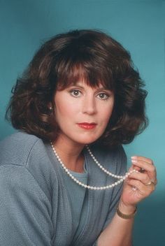 a woman wearing a pearl necklace posing for a photo in front of a blue background