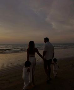 a man and woman holding hands while walking along the beach with their two children at sunset