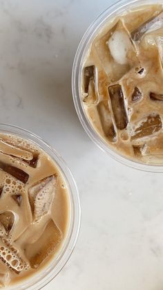 two cups filled with liquid and ice on top of a white counter next to each other