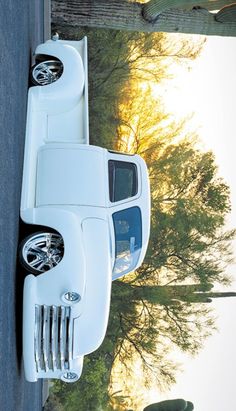 a white car parked on the side of a road next to a tree and fence