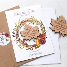 two wooden save the dates cards with maple leaves and flowers on them, sitting next to each other