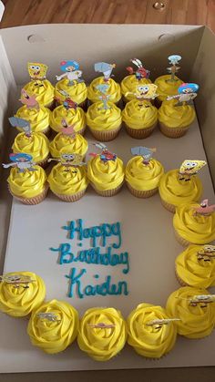 a box filled with yellow frosted cupcakes covered in frosting and cartoon characters