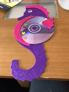 a purple and pink seahorse shaped cd case sitting on top of a wooden table