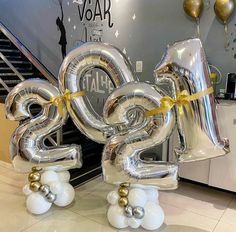 two large silver balloons in the shape of numbers are tied with gold ribbon and sitting on top of each other