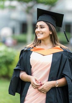 a woman wearing a graduation cap and gown standing in the grass with her hand on her hip