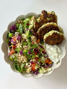 a white bowl filled with salad and meat patties next to a side of dressing