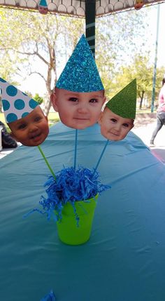 a table topped with three little kids wearing party hats and holding blue pom poms