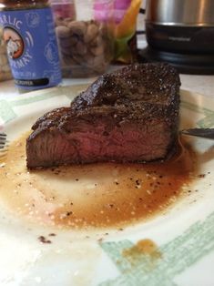 a piece of steak is on a plate with sauce and a fork next to it