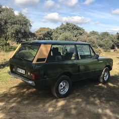 an old green station wagon parked on the side of a dirt road with trees in the background