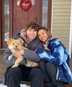 a man and woman are sitting on the porch with their dog in front of them