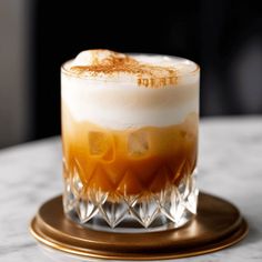 an orange and white drink sitting on top of a marble table next to a gold plate