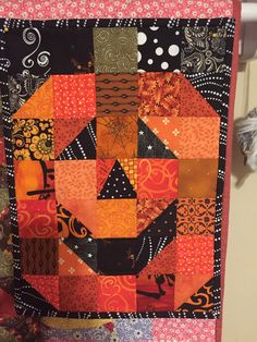 an orange and black patchwork quilt hanging on a wall