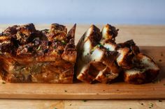 a wooden cutting board topped with slices of bread covered in meat and cheese toppings