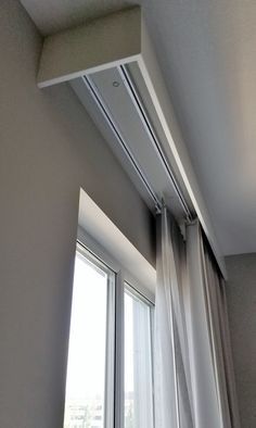 an open window with white curtains in front of it and a curtain rod hanging from the ceiling