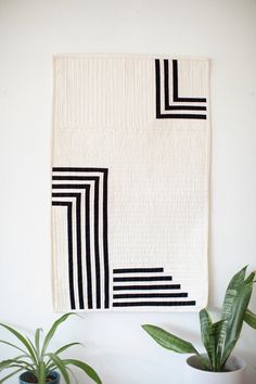 a black and white wall hanging next to two potted plants