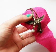 a hand holding a pink flower with a chain attached to it