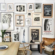 a room filled with lots of framed pictures and art hanging on the wall next to a wooden table