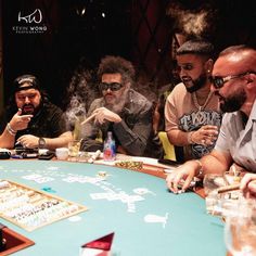 four men sitting at a table with cigars in their hands and playing cards on the table