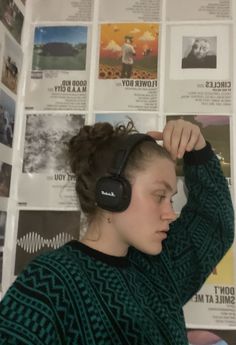 a woman wearing headphones standing in front of a wall covered with pictures and posters