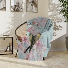 a chair covered in a floral blanket next to a potted plant and pictures on the wall