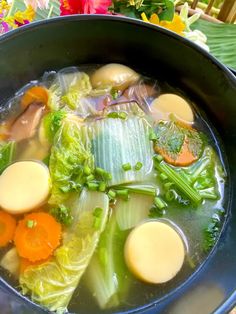 a pot filled with soup and vegetables on top of a wooden table next to flowers