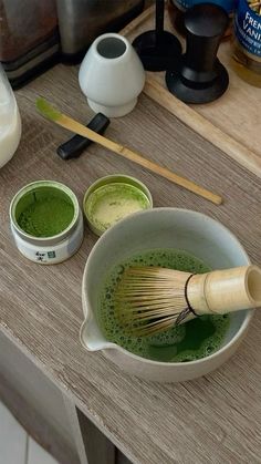 a wooden table topped with bowls filled with green liquid and whisk in them