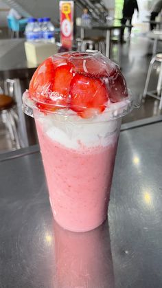 a strawberry smoothie in a plastic cup with strawberries on the top, sitting on a table