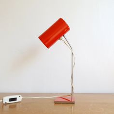 a red lamp sitting on top of a wooden table next to a white phone charger