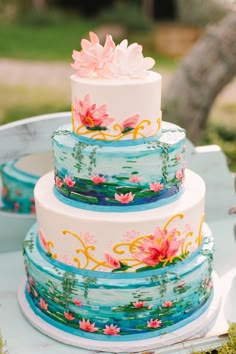 a three tiered cake decorated with flowers and water lillies on a table outside