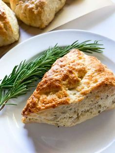 a piece of bread on a white plate next to rosemary sprigs and some biscuits