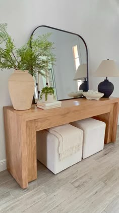 a wooden table topped with a mirror and two stools next to a potted plant