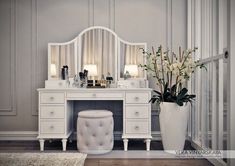 a white dressing table with a mirror and stool next to a vase filled with flowers