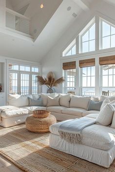 a living room filled with lots of white furniture and large windows above the couches